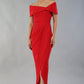 model wearing diva catwalk vegas calf length midaxi dress with wide bardot neckline and open shoulders with a large opening at the front of the skirt with pleating coming down long skirt front in scarlet red