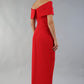 model wearing diva catwalk vegas calf length midaxi dress with wide bardot neckline and open shoulders with a large opening at the front of the skirt with pleating coming down long skirt front in scarlet red