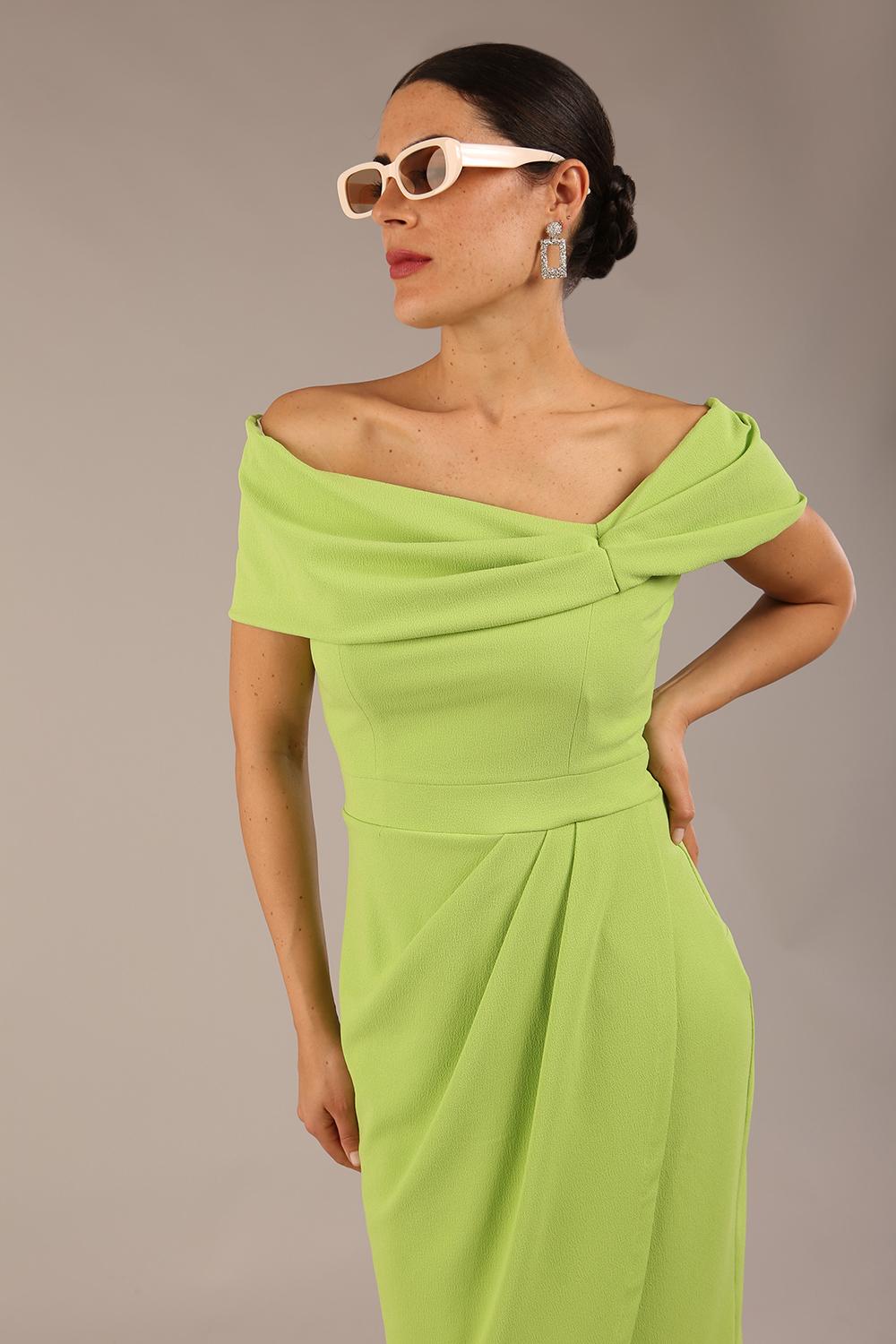 brunette model wearing diva catwalk vegas calf length lime green midaxi dress with wide bardot neckline and open shoulders with a large opening at the front of the skirt with pleating coming down long skirt front 