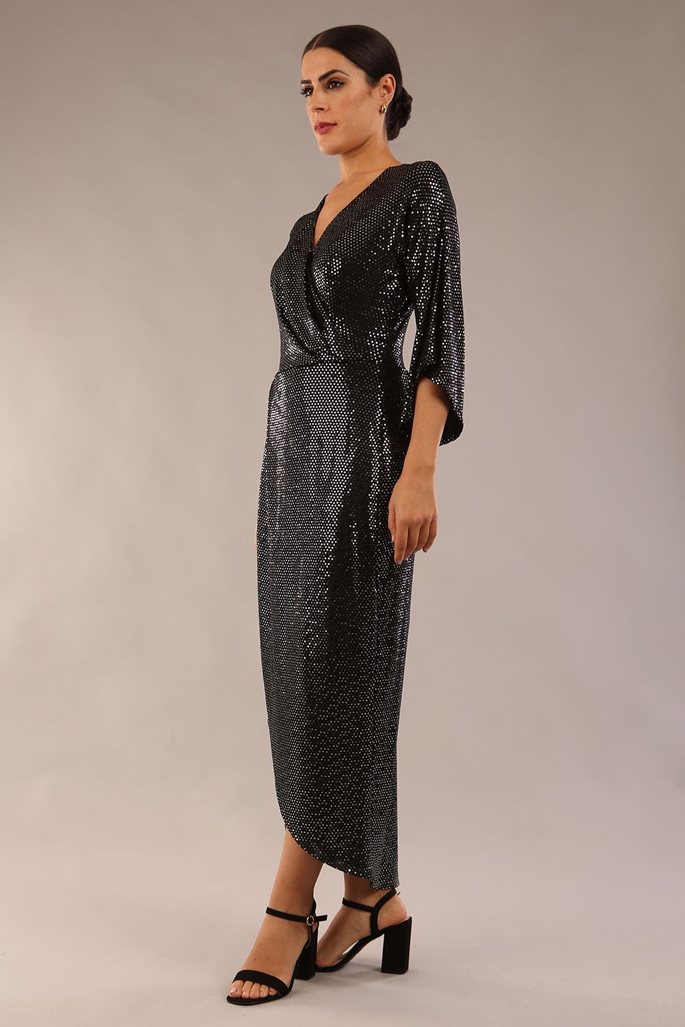 Brunette model wearing diva catwalk Glitterati Midaxi Sparkle Dress in Black in Jersey sparkle and ITY lining with wrap dress style and 3/4 length bell sleeves front side