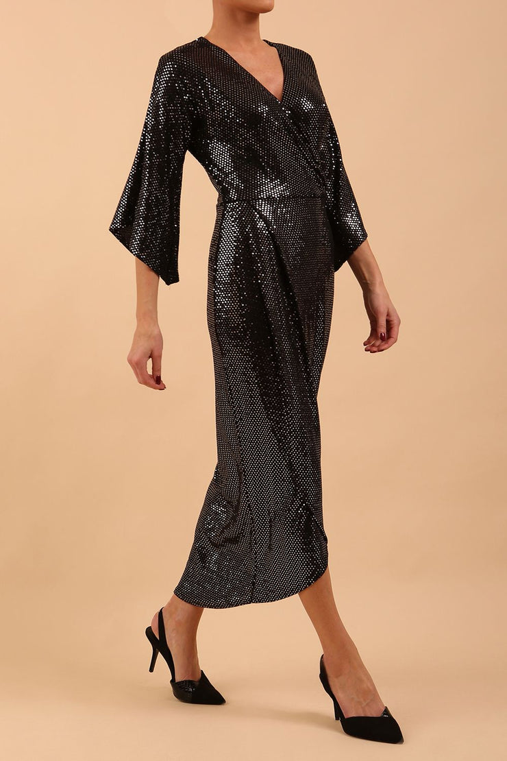 Brunette model wearing diva catwalk Glitterati Midaxi Sparkle Dress in Black in Jersey sparkle and ITY lining with wrap dress style and 3/4 length bell sleeves front side