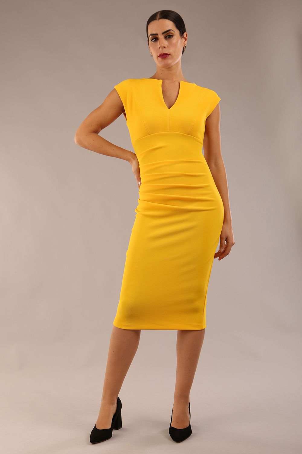 brunette model wearing diva catwalk lydia sleeveless pencil flattering fitted plain dress with split neckline and pleating across the body in spectra yellow front