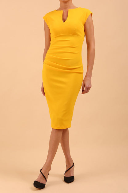 brunette model wearing diva catwalk lydia sleeveless pencil flattering fitted plain dress with split neckline and pleating across the body in spectra yellow front