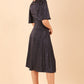 brunette model wearing diva catwalk cambrian satin swing dress with bell short sleeve wide asymmetric waistband and pleating under bust and low v-neckline in navy back