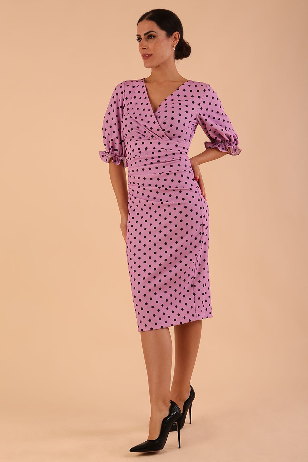 brunette model wearing diva catwalk palacio pencil fitted dress with three quarter puffed sleeve and pleating across the body with overlapping v-neckline in pink polka dot front