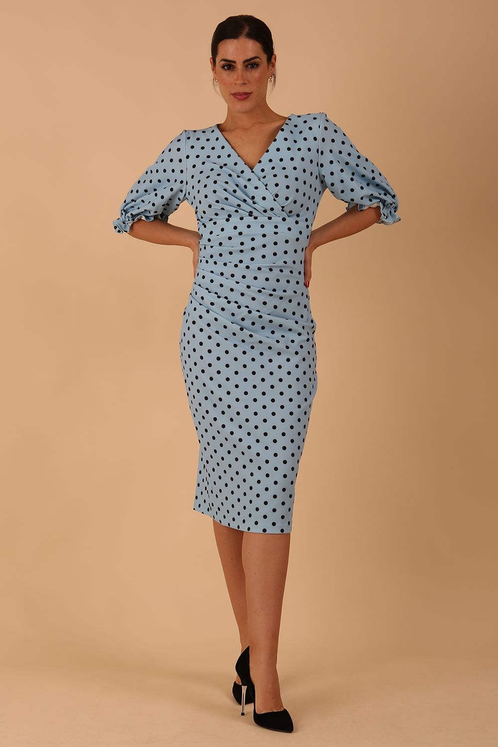  model wearing Diva Catwalk Palacio Pencil dress v neckline and pleating across the tummy with puffed short sleeves in blue polka dot front