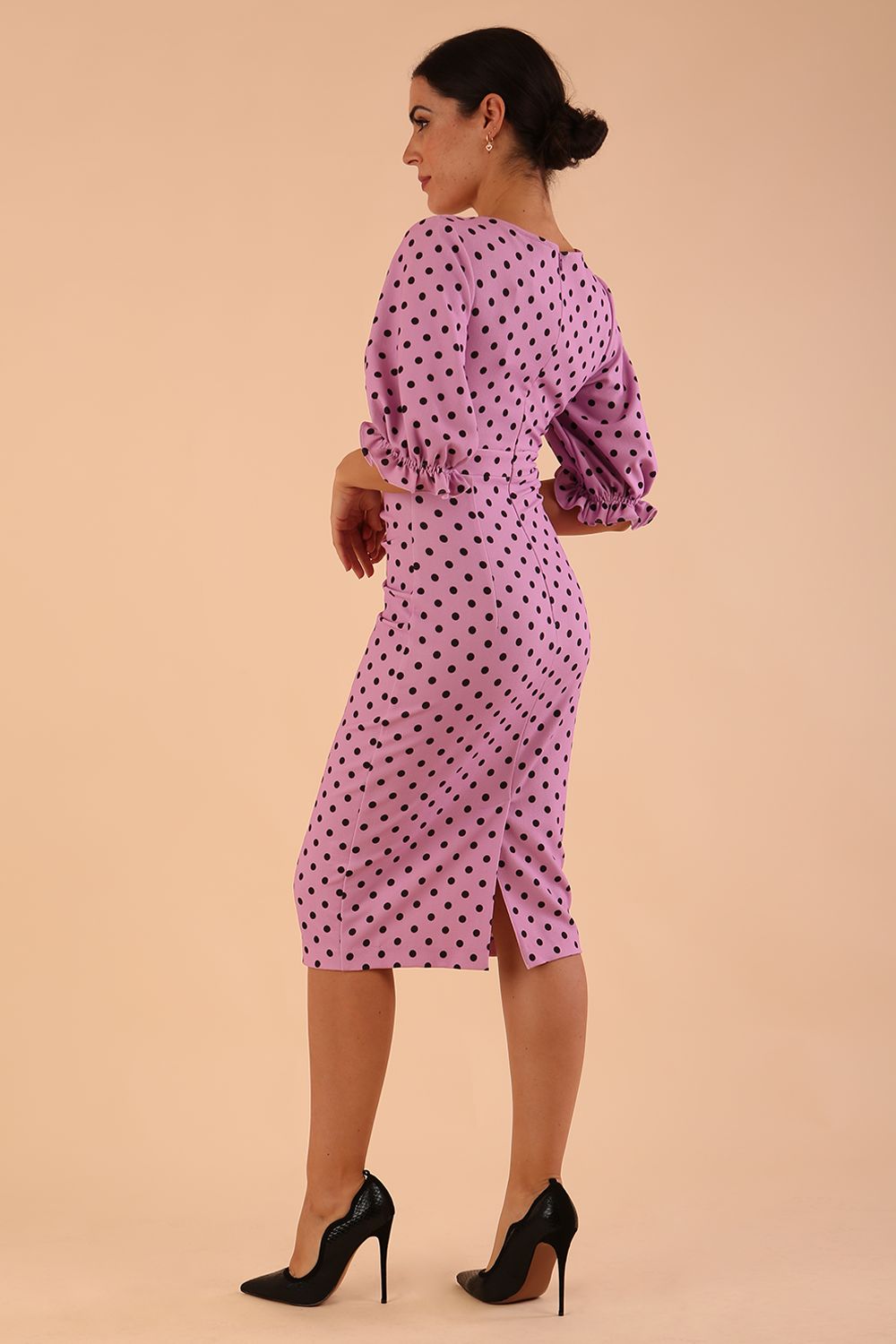 brunette model wearing diva catwalk palacio pencil fitted dress with three quarter puffed sleeve and pleating across the body with overlapping v-neckline in pink polka dot back