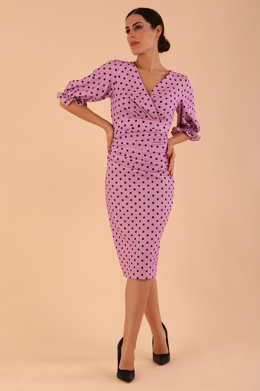brunette model wearing diva catwalk palacio pencil fitted dress with three quarter puffed sleeve and pleating across the body with overlapping v-neckline in pink polka dot front