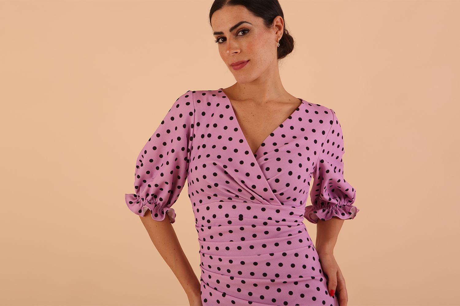 brunette model wearing diva catwalk palacio pencil fitted dress with three quarter puffed sleeve and pleating across the body with overlapping v-neckline in pink polka dot front close up