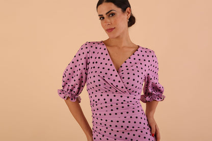 brunette model wearing diva catwalk palacio pencil fitted dress with three quarter puffed sleeve and pleating across the body with overlapping v-neckline in pink polka dot front close up