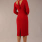 brunette model wearing diva catwalk wimpole a-line flattering dress with lowered v-neck and three quarter sleeve and cinching waistband and widened skirt with pleating in scarlet red back