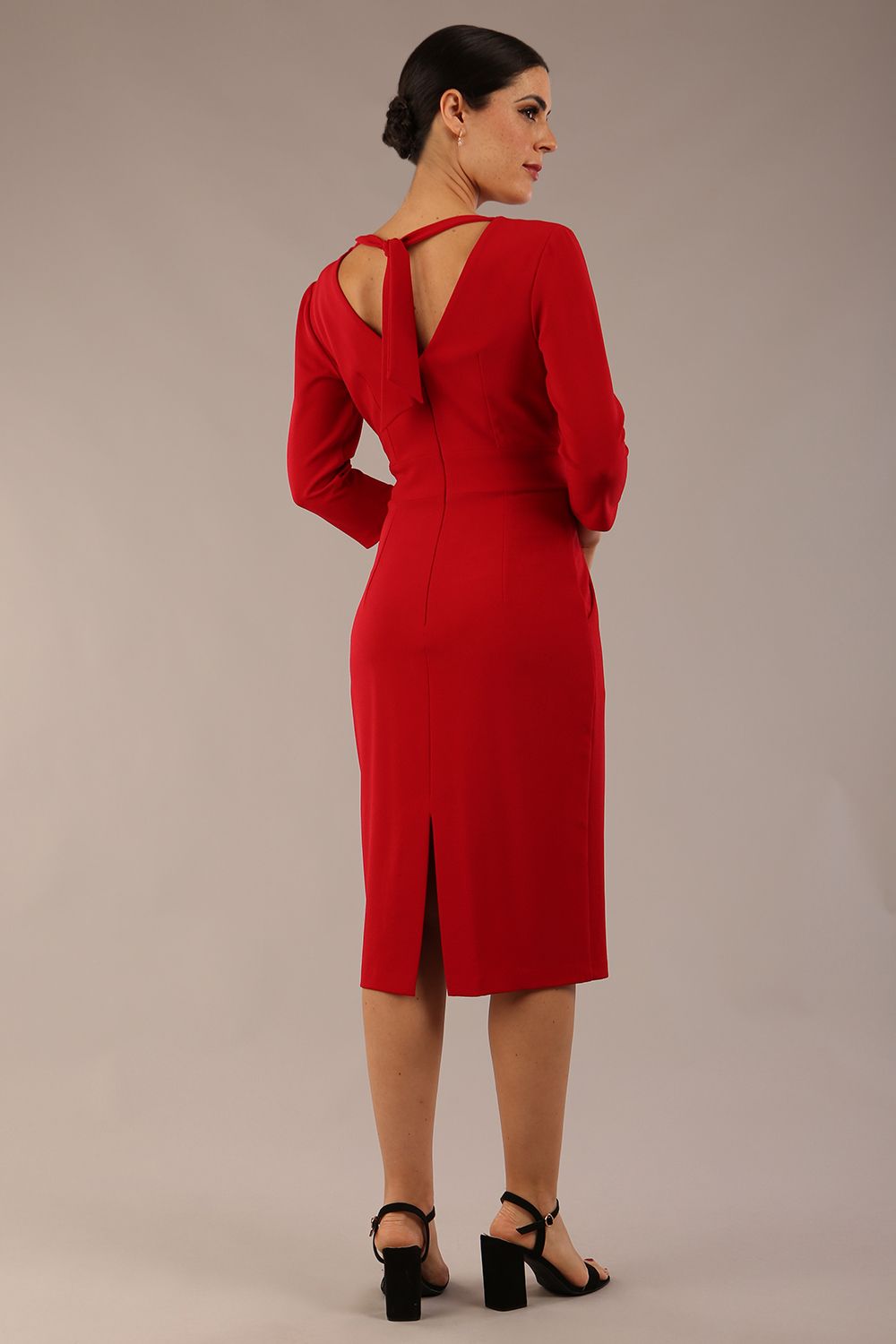 brunette model wearing diva catwalk wimpole a-line flattering dress with lowered v-neck and three quarter sleeve and cinching waistband and widened skirt with pleating in scarlet red back