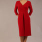 brunette model wearing diva catwalk wimpole a-line flattering dress with lowered v-neck and three quarter sleeve and cinching waistband and widened skirt with pleating in scarlet red front