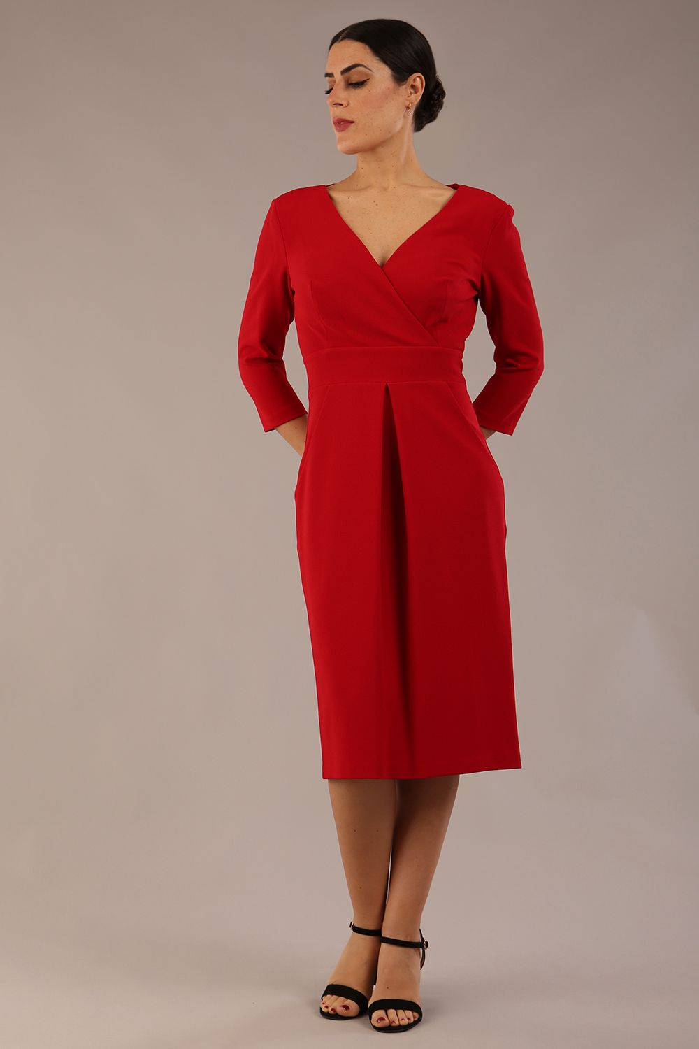 brunette model wearing diva catwalk wimpole a-line flattering dress with lowered v-neck and three quarter sleeve and cinching waistband and widened skirt with pleating in scarlet red front