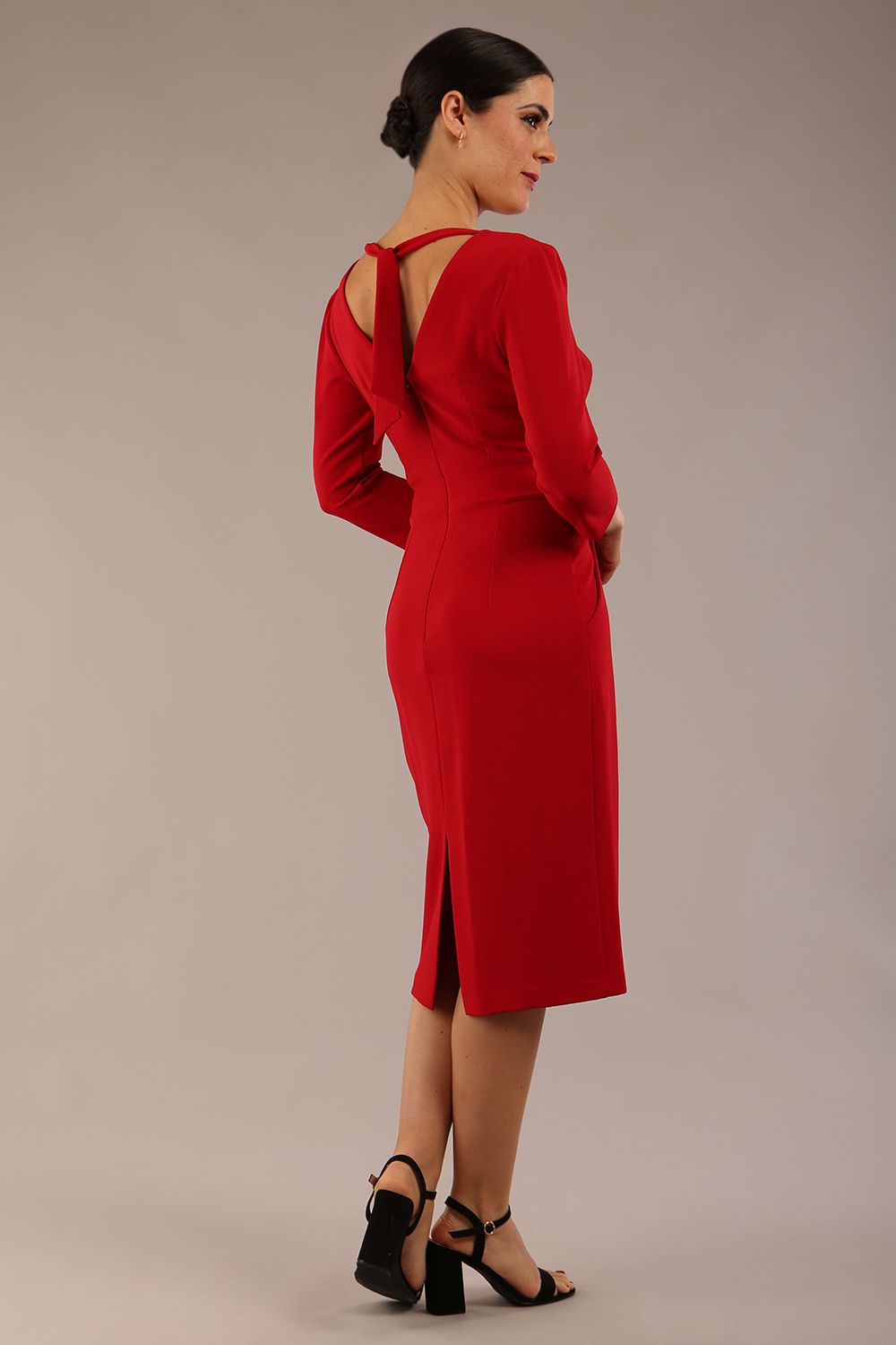 brunette model wearing diva catwalk wimpole a-line flattering dress with lowered v-neck and three quarter sleeve and cinching waistband and widened skirt with pleating in scarlet red back side