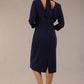 brunette model wearing diva catwalk wimpole a-line flattering dress with lowered v-neck and three quarter sleeve and cinching waistband and widened skirt with pleating in navy blue back