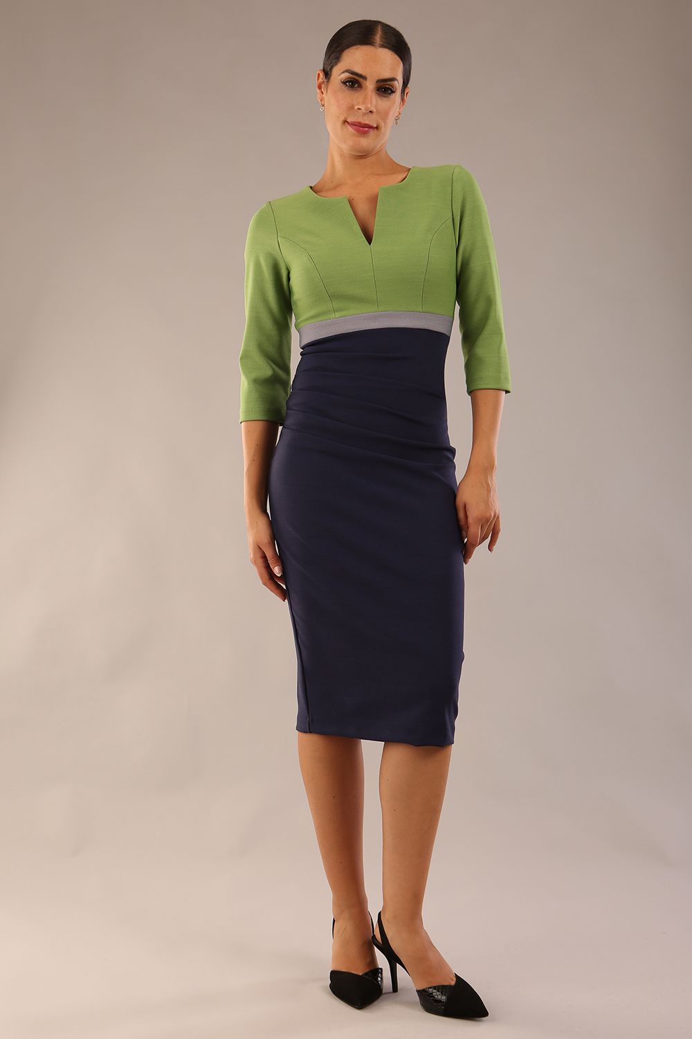 brunette model wearing seed lara pencil colour block dress three quarter sleeve and pleating across the body with split neckline in navy blue and citrus green and sky grey front