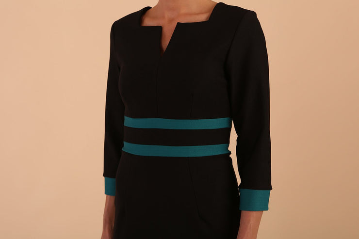 brunette model wearing Diva catwalk Paeonia dress square neckline with a vent in black with Pacific Green and black stripes around the waist and three quarter sleeve with Pacific Green contrast finish detail