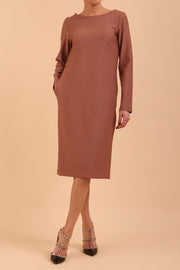brunette model wearing diva catwalk cora white pencil dress with long sleeves and rounded neckline with pockets in colour acorn brown on  front