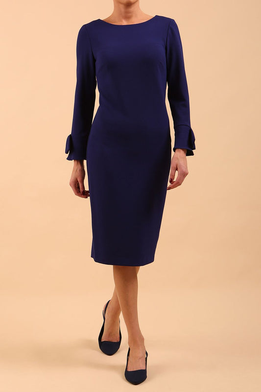 brunette model wearing diva catwalk fitted dress with sleeves called Alma Pencil-skirt dress in colour oxford blue with bow detail on sleeves front