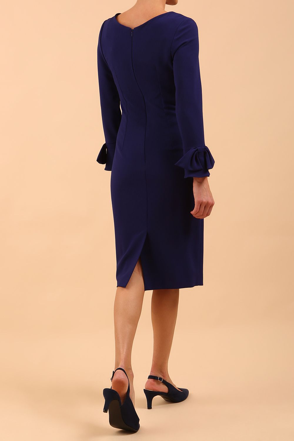 brunette model wearing diva catwalk fitted dress with sleeves called Alma Pencil-skirt dress in colour oxford blue with bow detail on sleeves back