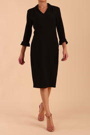 brunette model wearing diva catwalk adriana pencil dress with low v-neck and pleating around shoulders with three quarter sleeve detailed on end and wide waistband in black front