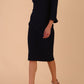 brunette model wearing diva catwalk adriana pencil dress with low v-neck and pleating around shoulders with three quarter sleeve detailed on end and wide waistband in dark navy front side
