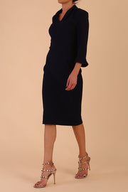 brunette model wearing diva catwalk adriana pencil dress with low v-neck and pleating around shoulders with three quarter sleeve detailed on end and wide waistband in dark navy front side