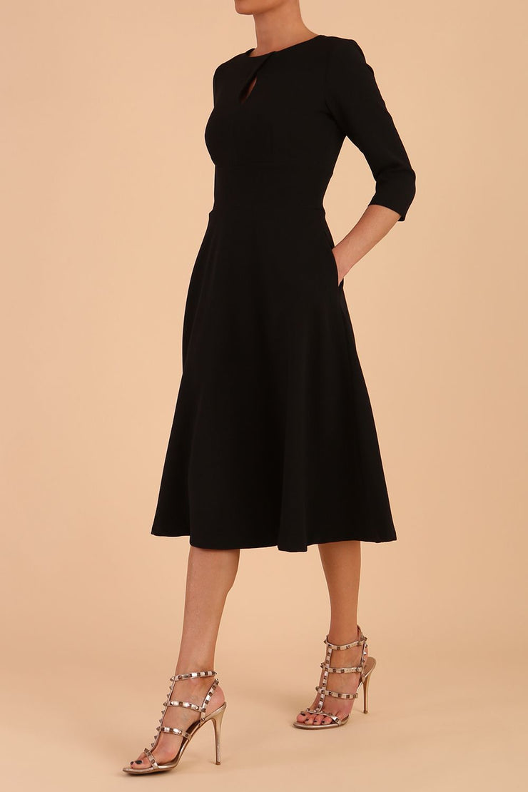 Brunette model is wearing diva catwalk casares swing dress with a keyhole neckline three quarter sleeve dress with pocket detail in black front side