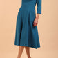 A brunette model is wearing a swing teal three quarter sleeve dress with oversized collar and pockets in the skirt