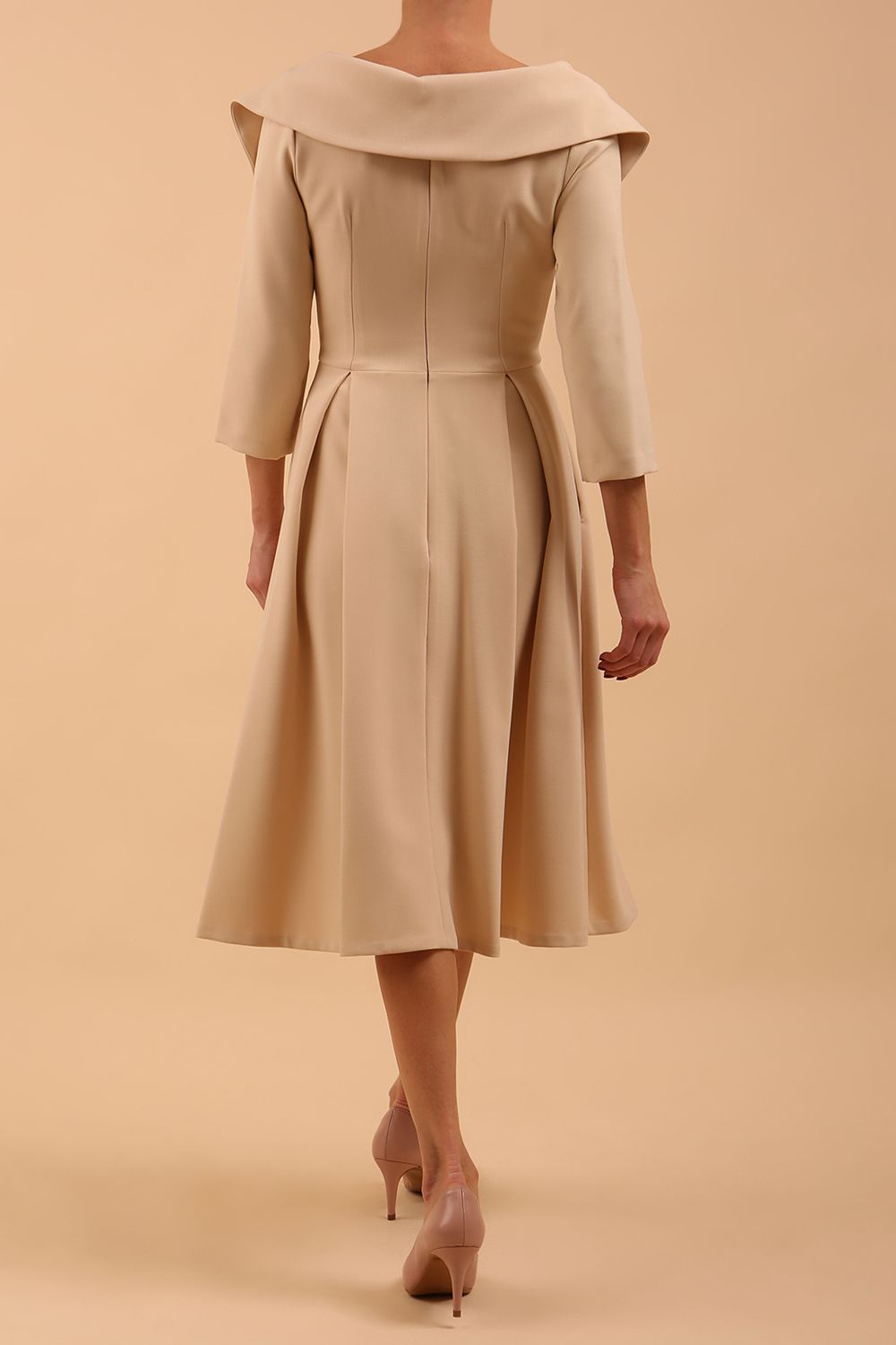Brunette model is wearing a sleeved sandshell beige oversized collar swing dress with button detail at the front and pockets in the skirt