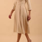 Brunette model is wearing a sleeved sandshell beige oversized collar swing dress with button detail at the front and pockets in the skirt