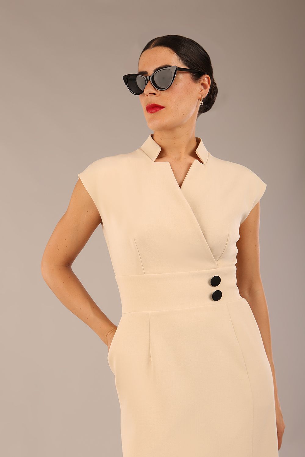 brunette Model is wearing a diva catwalk Derby pencil skirt dress cap sleeves with buttons details at the waistband and star neckline below the knee length with pockets in sandshell beige colour front image 