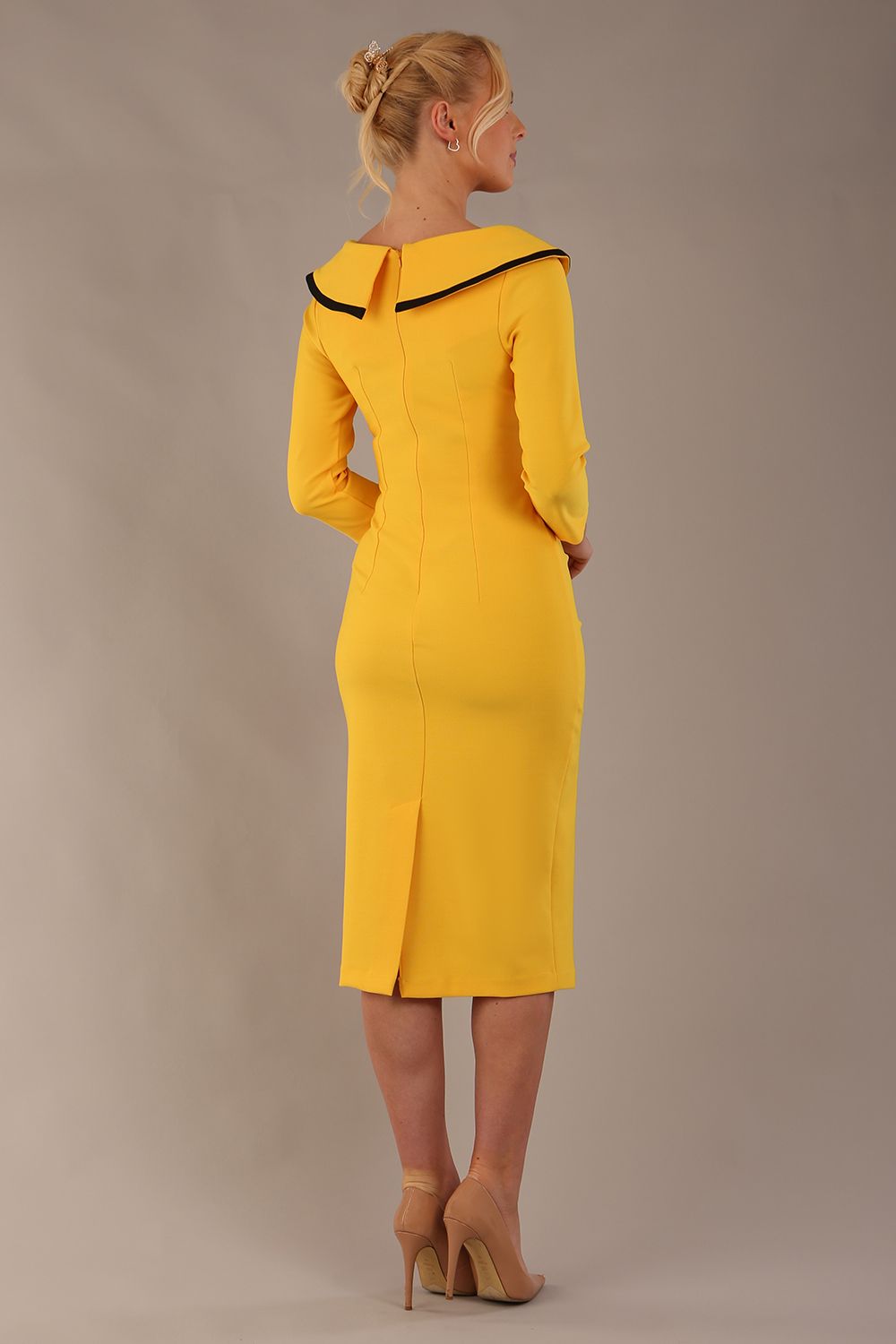 Model wearing diva catwalk Seed Elsye 3/4 Sleeve Knee Length Pencil Dress with Fold over bateau collar neckline with contrast piping and Bow feature on the left side of the bodice with decorative brooch in Daffodil Yellow colour back (Daffodil Yellow / Black Contrast)