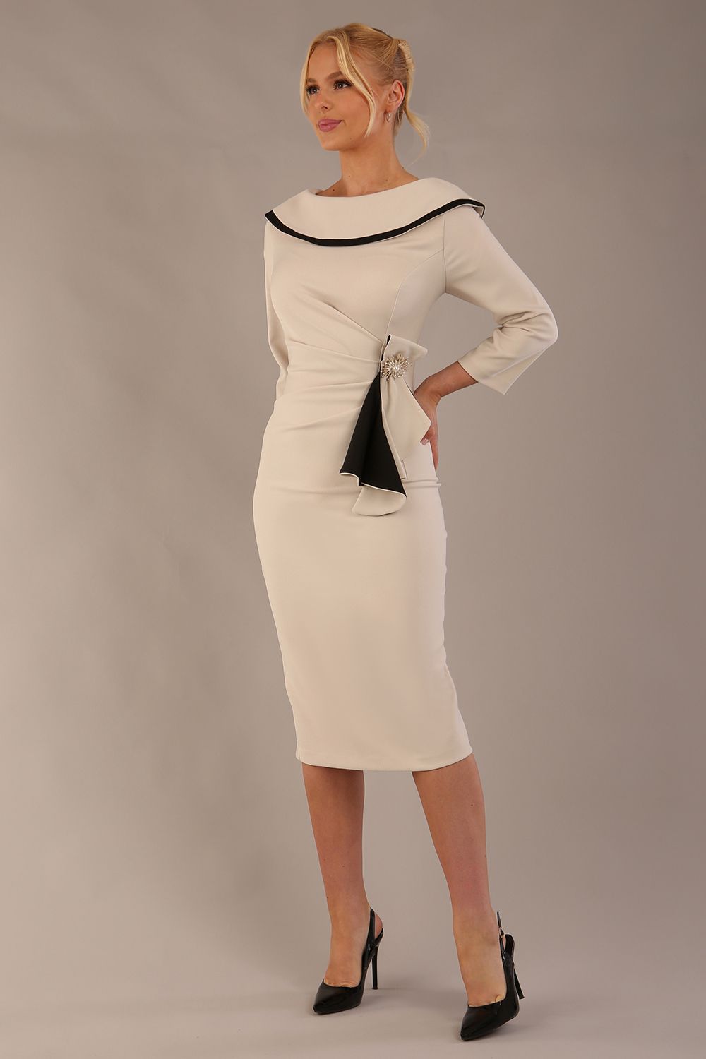 Model wearing diva catwalk Seed Elsye 3/4 Sleeve Knee Length Pencil Dress with Fold over bateau collar neckline with contrast piping and Bow feature on the left side of the bodice in Sandy Cream colour front side (Sandy Cream / Black Contrast)