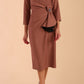 Model wearing diva catwalk Seed  Elsye 3/4 Sleeve Knee Length Pencil Dress with Fold over bateau collar neckline with contrast piping and Bow feature on the left side of the bodice with decorative brooch in Acorn Brown colour front