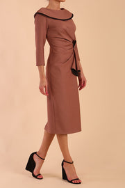 Model wearing diva catwalk Seed  Elsye 3/4 Sleeve Knee Length Pencil Dress with Fold over bateau collar neckline with contrast piping and Bow feature on the left side of the bodice with decorative brooch in Acorn Brown colour front side