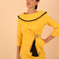 odel wearing diva catwalk Seed Elsye 3/4 Sleeve Knee Length Pencil Dress with Fold over bateau collar neckline with contrast piping and Bow feature on the left side of the bodice with decorative brooch in Daffodil Yellow close up colour front