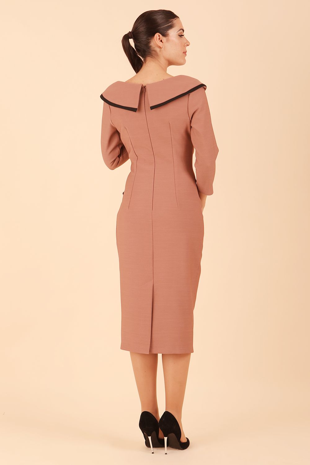 Model wearing diva catwalk Seed Elsye 3/4 Sleeve Knee Length Pencil Dress with Fold over bateau collar neckline with contrast piping and Bow feature on the left side of the bodice with decorative brooch in Acorn Brown colour back