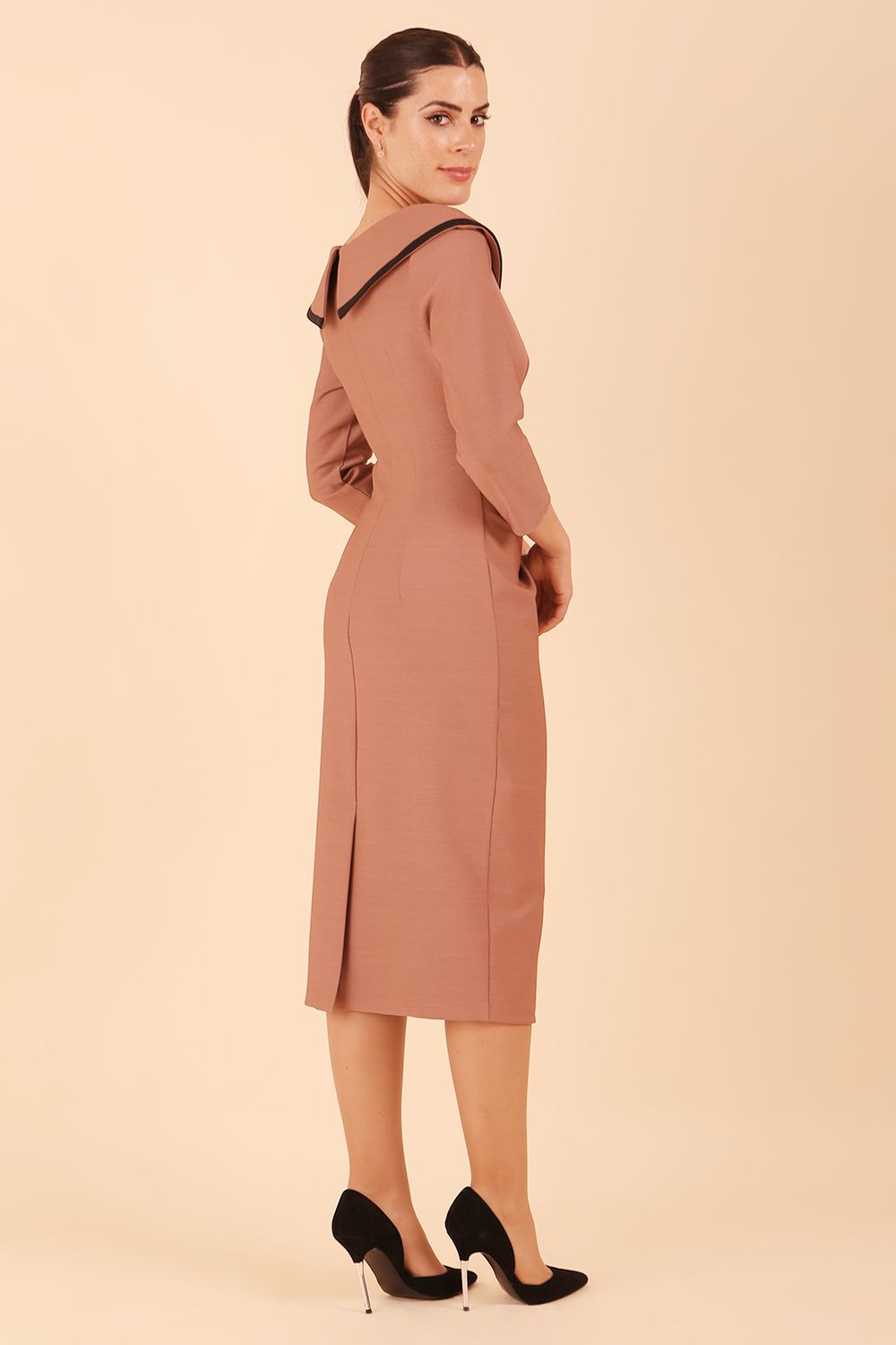 Model wearing diva catwalk Seed Elsye 3/4 Sleeve Knee Length Pencil Dress with Fold over bateau collar neckline with contrast piping and Bow feature on the left side of the bodice with decorative brooch in Acorn Brown colour back side