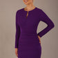 model wearing a diva catwalk lydia long sleeved pleated Mini Dress from Diva Catwalk in passion purple in high heal shoes against a beige background close up