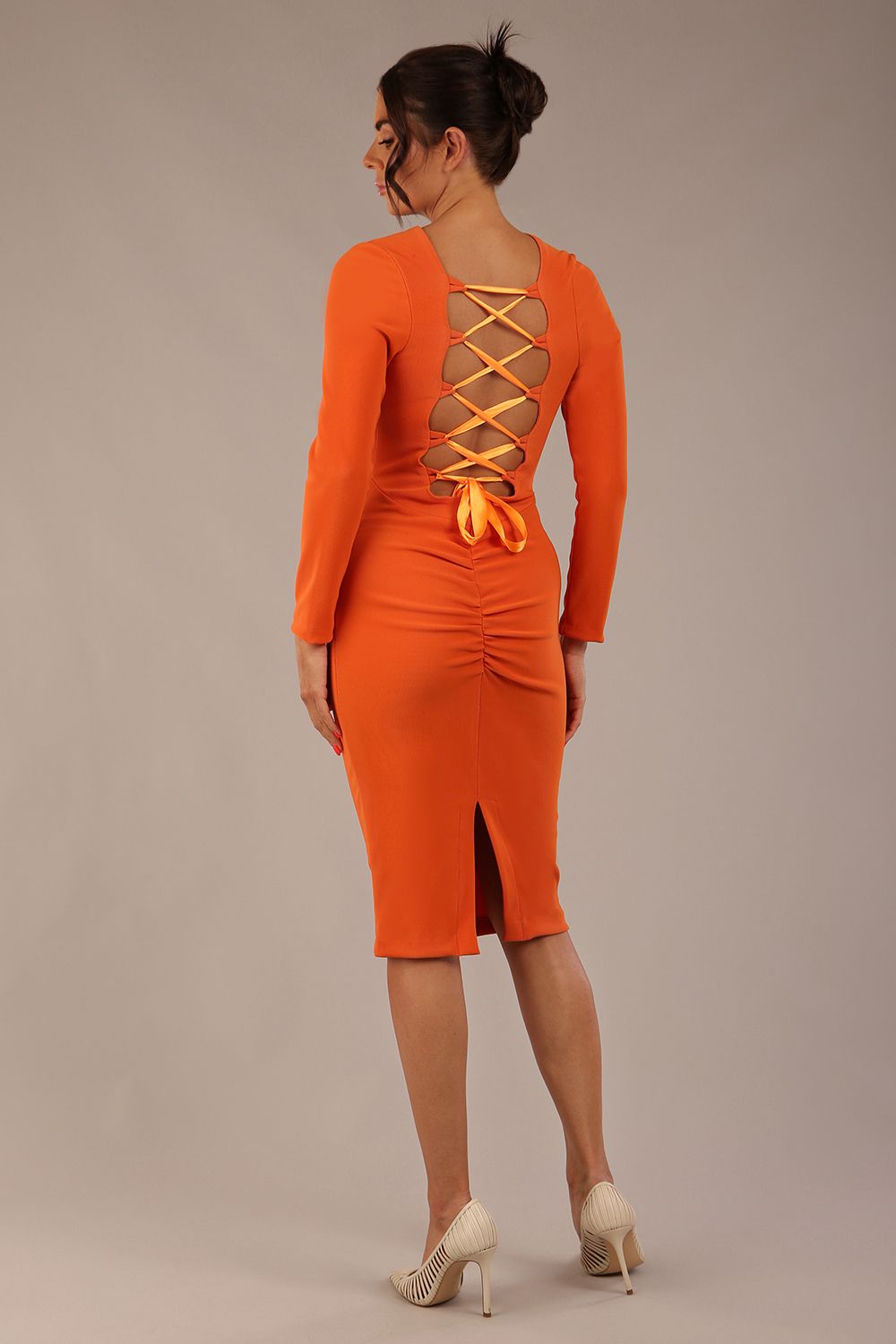 brunette model wearing a diva catwalk Zoey Sleeved Pencil Dress ribbon back with long sleeves and rushed details front and back in Amber Orange colour back