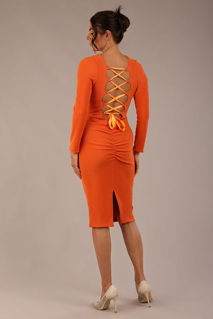 brunette model wearing a diva catwalk Zoey Sleeved Pencil Dress ribbon back with long sleeves and rushed details front and back in Amber Orange colour back