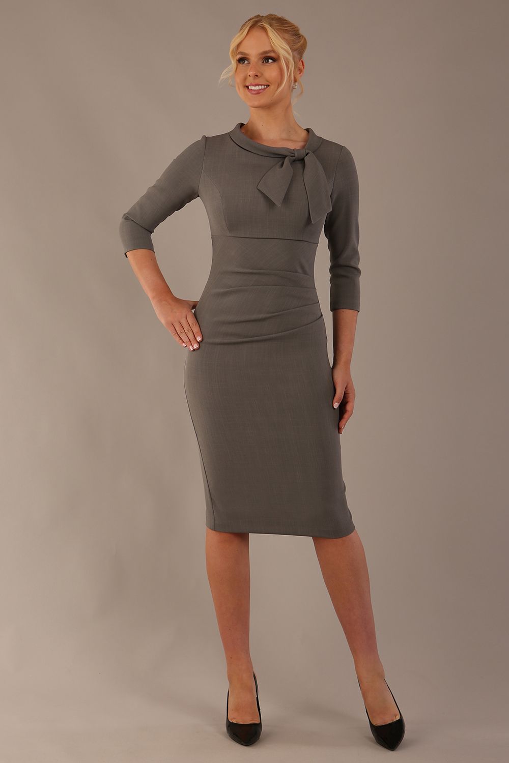 The model is wearing a diva catwalk Juliette 3/4 Sleeve Knee Length dress with bow detail in castlerock grey colour against a plain background