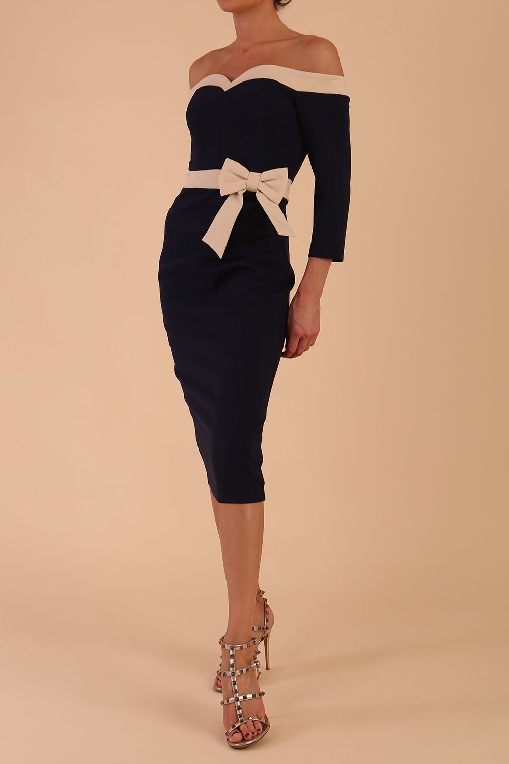 Model wearing a diva catwalk Brittany Off Shoulder Bow detail Pencil Dress with 3/4 sleeves and knee length in Navy Blue and Sandshell Beige colour front side 
