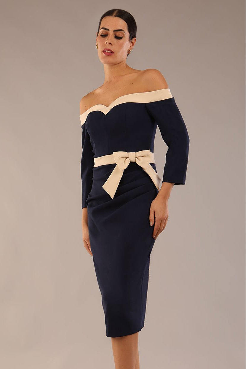 Model wearing a diva catwalk Brittany Off Shoulder Bow detail Pencil Dress with 3/4 sleeves and knee length in Navy Blue and Sandshell Beige colour front side