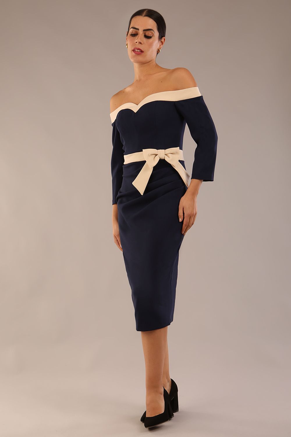 Model wearing a diva catwalk Brittany Off Shoulder Bow detail Pencil Dress with 3/4 sleeves and knee length in Navy Blue and Sandshell Beige colour front side