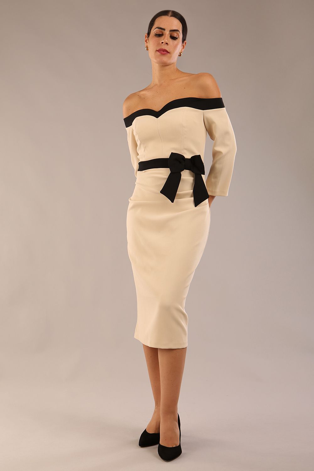 Model wearing a diva catwalk Brittany Off Shoulder Bow detail Pencil Dress with 3/4 sleeves and knee length in Sandshell Beige and Black colour 