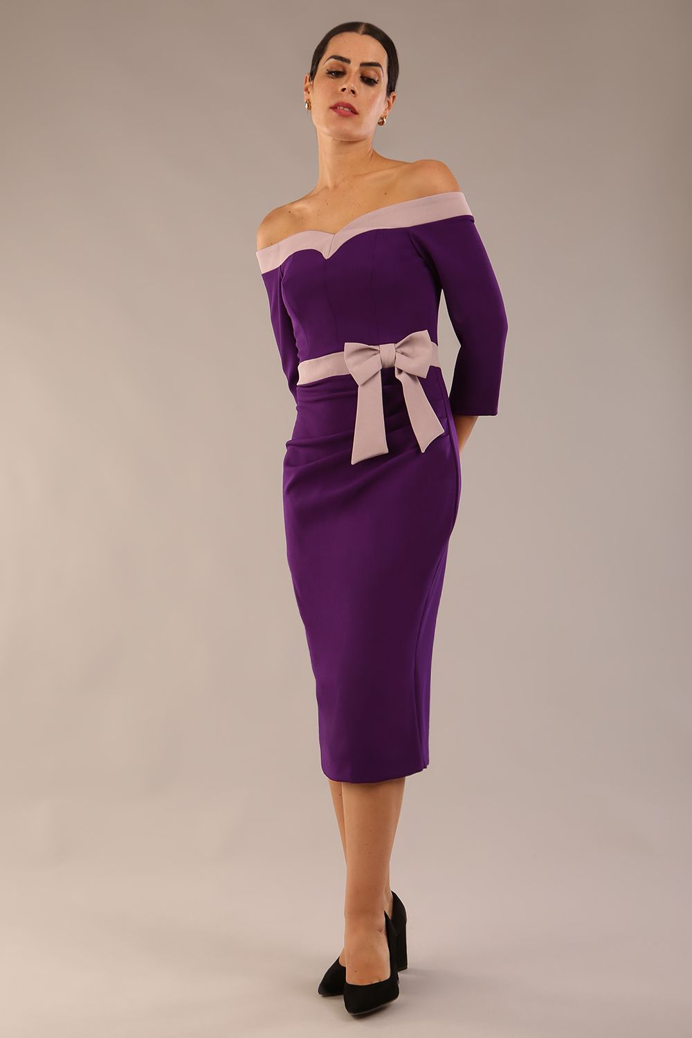 Model wearing a diva catwalk Brittany Off Shoulder Bow detail Pencil Dress with 3/4 sleeves and knee length in Deep Purple and Thunder Bird colour