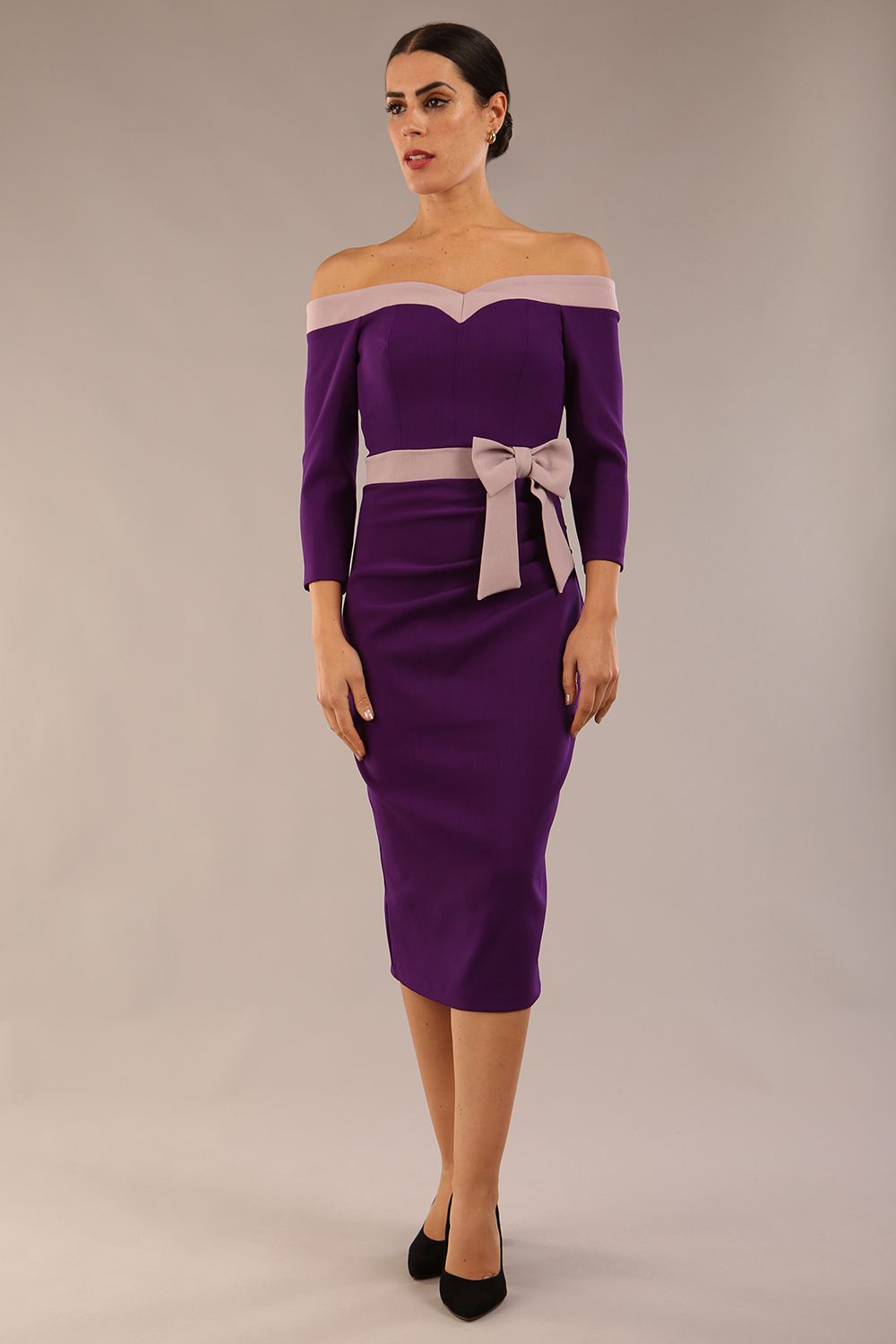 Model wearing a diva catwalk Brittany Off Shoulder Bow detail Pencil Dress with 3/4 sleeves and knee length in Deep Purple and Thunder Bird colour